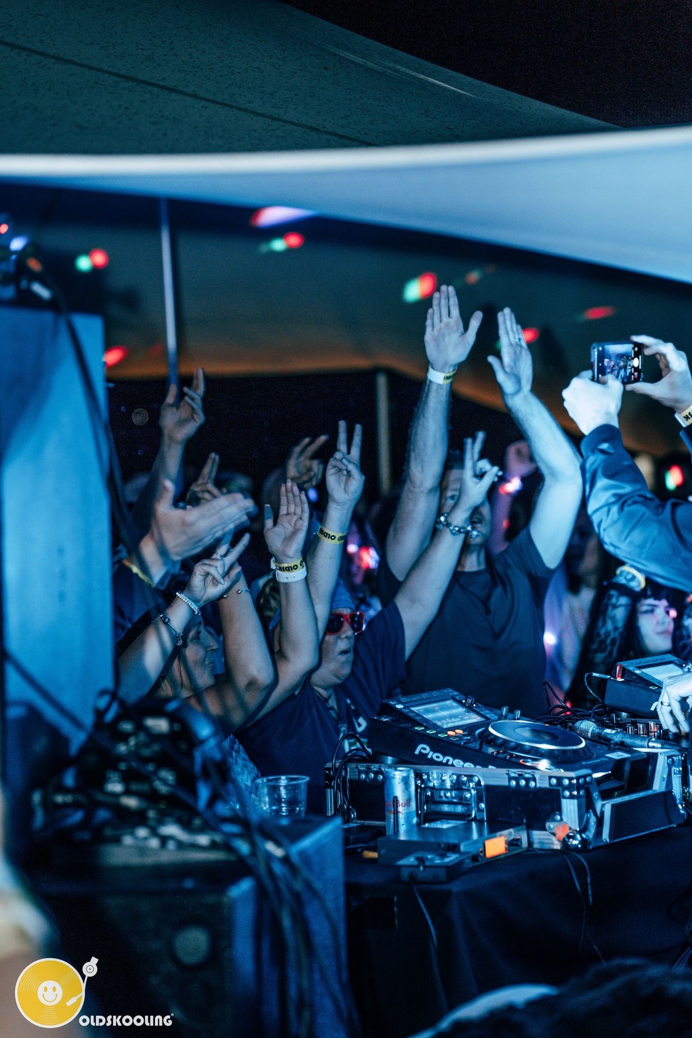 Crowd with raised hands at a nightclub DJ booth under blue lighting