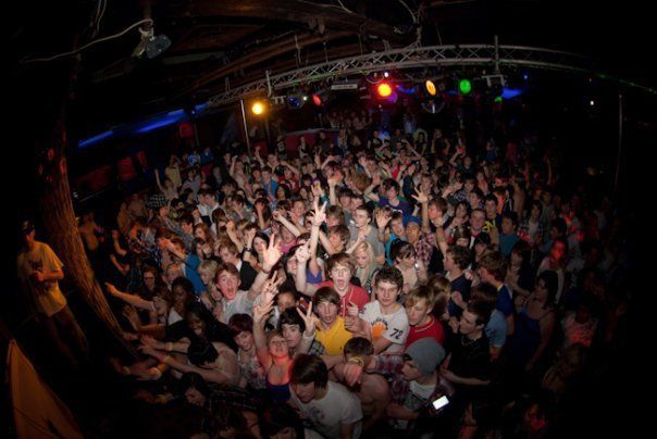 Crowded nightclub dance floor with a cheering crowd under colorful stage lights