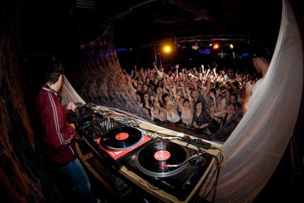 DJ performing at a nightclub with a crowd cheering under colorful lights
