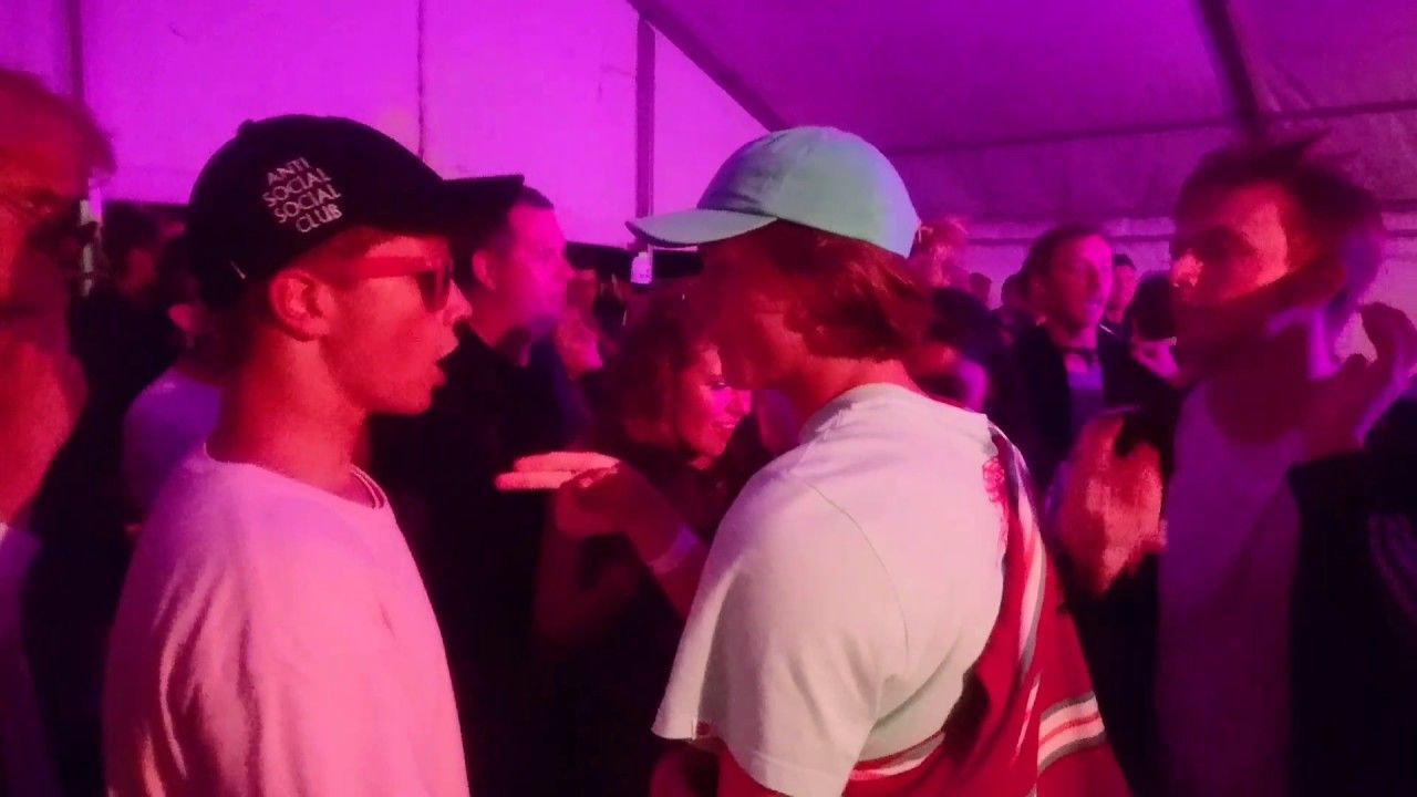 People standing closely in a purple-lit crowd at an indoor event, some wearing caps and casual shirts
