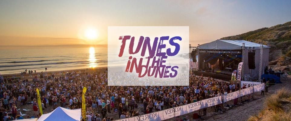 Sunset beach concert crowd with large “TUNES IN THE DUNES” sign near the stage