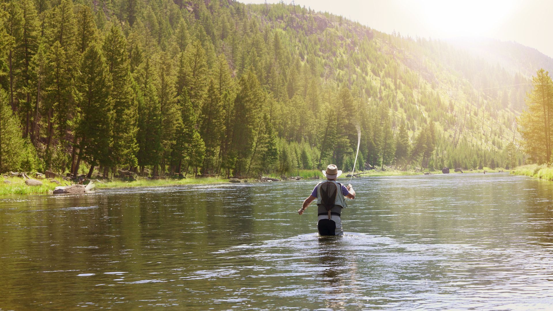 A man is fishing in a river with a fishing rod.