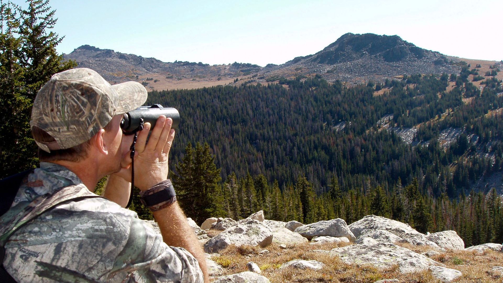 A man is looking through binoculars at a mountain range.