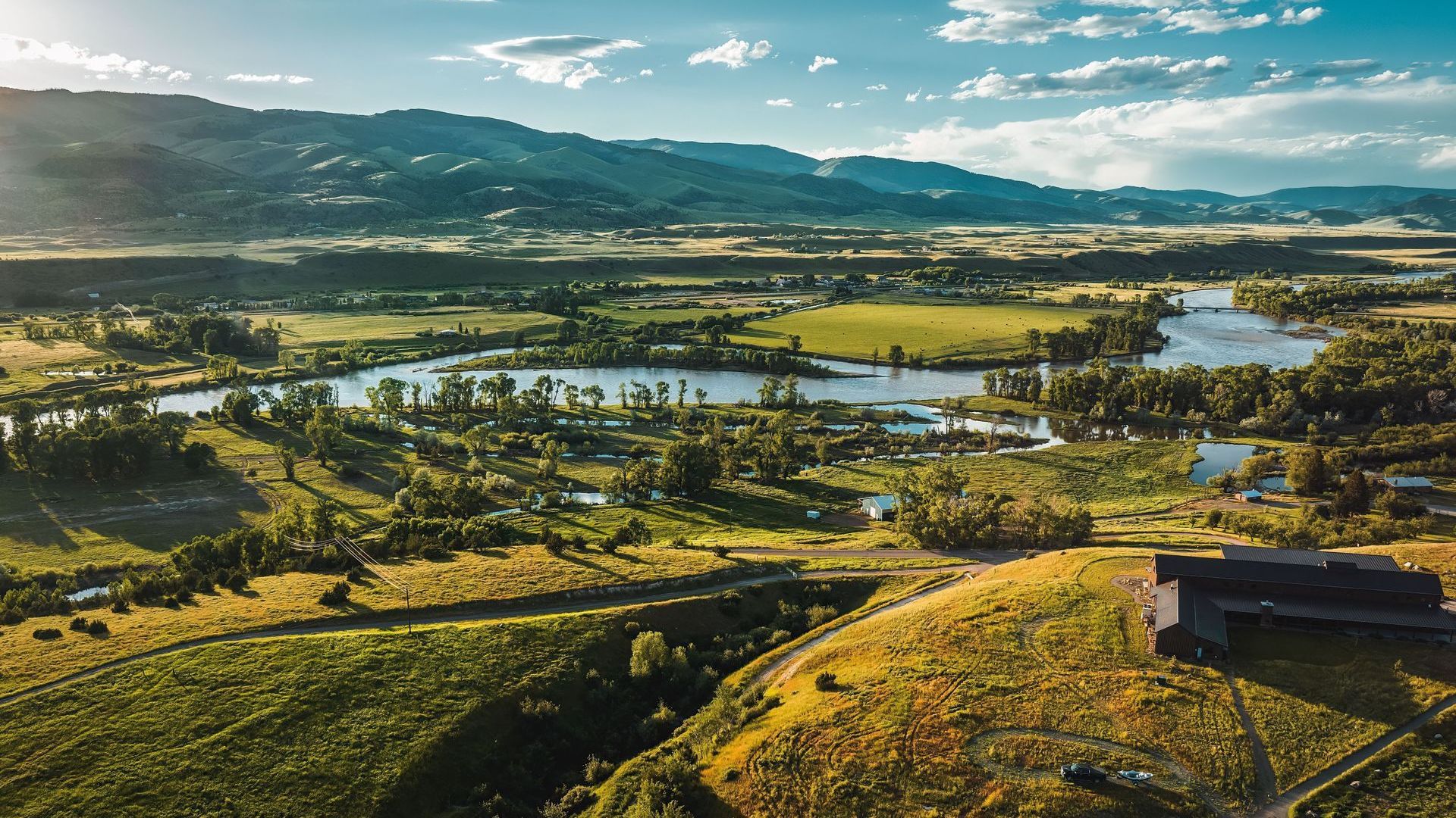 An aerial view of a valley with a river and mountains in the background.