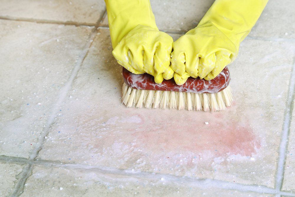 Yellow-gloved Hands Scrubbing a Tile Floor — Glittering Cleaning Service In Townsville, QLD