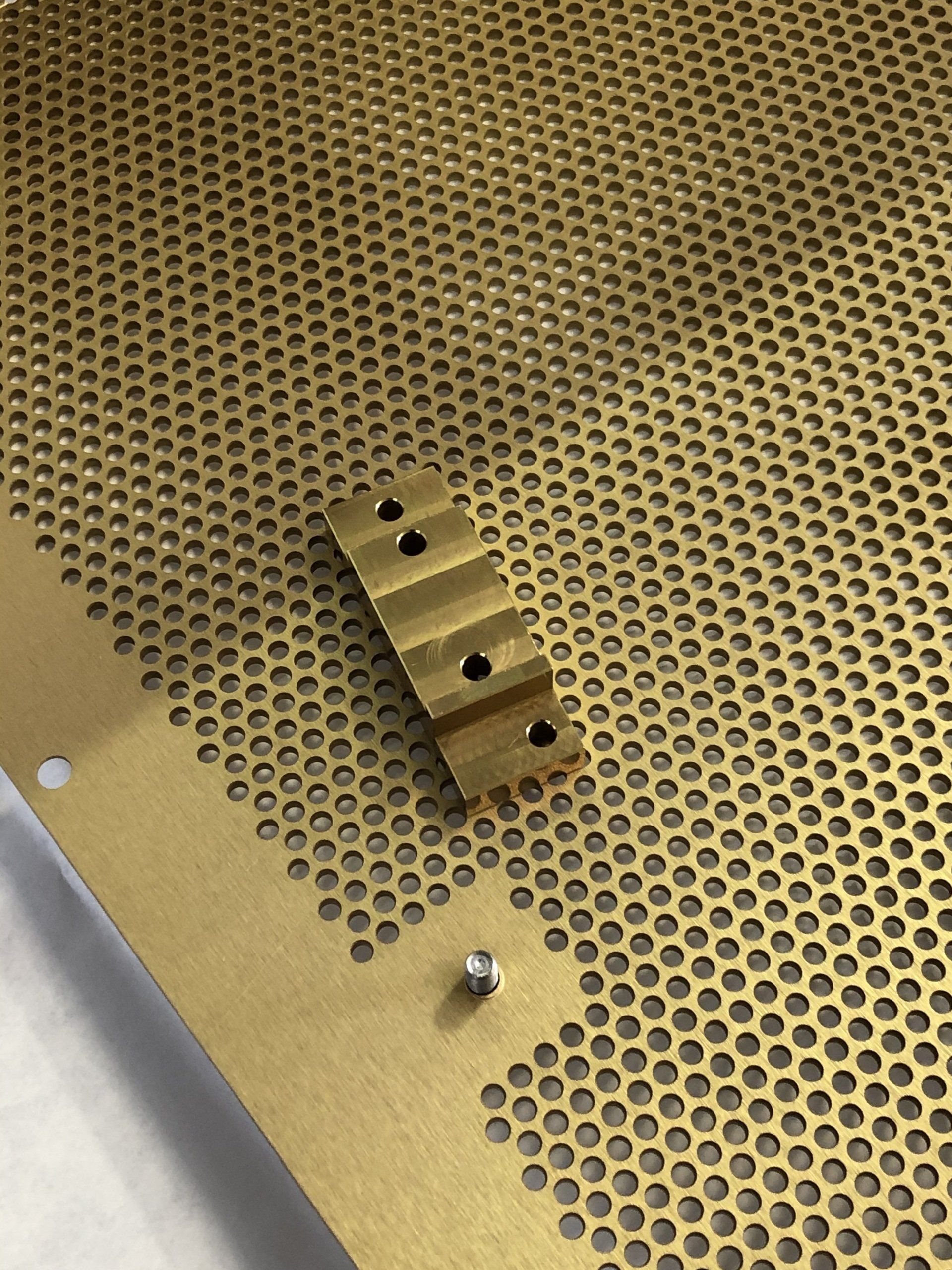 Perforated brass sheet with a gold-colored bracket and a silver screw.