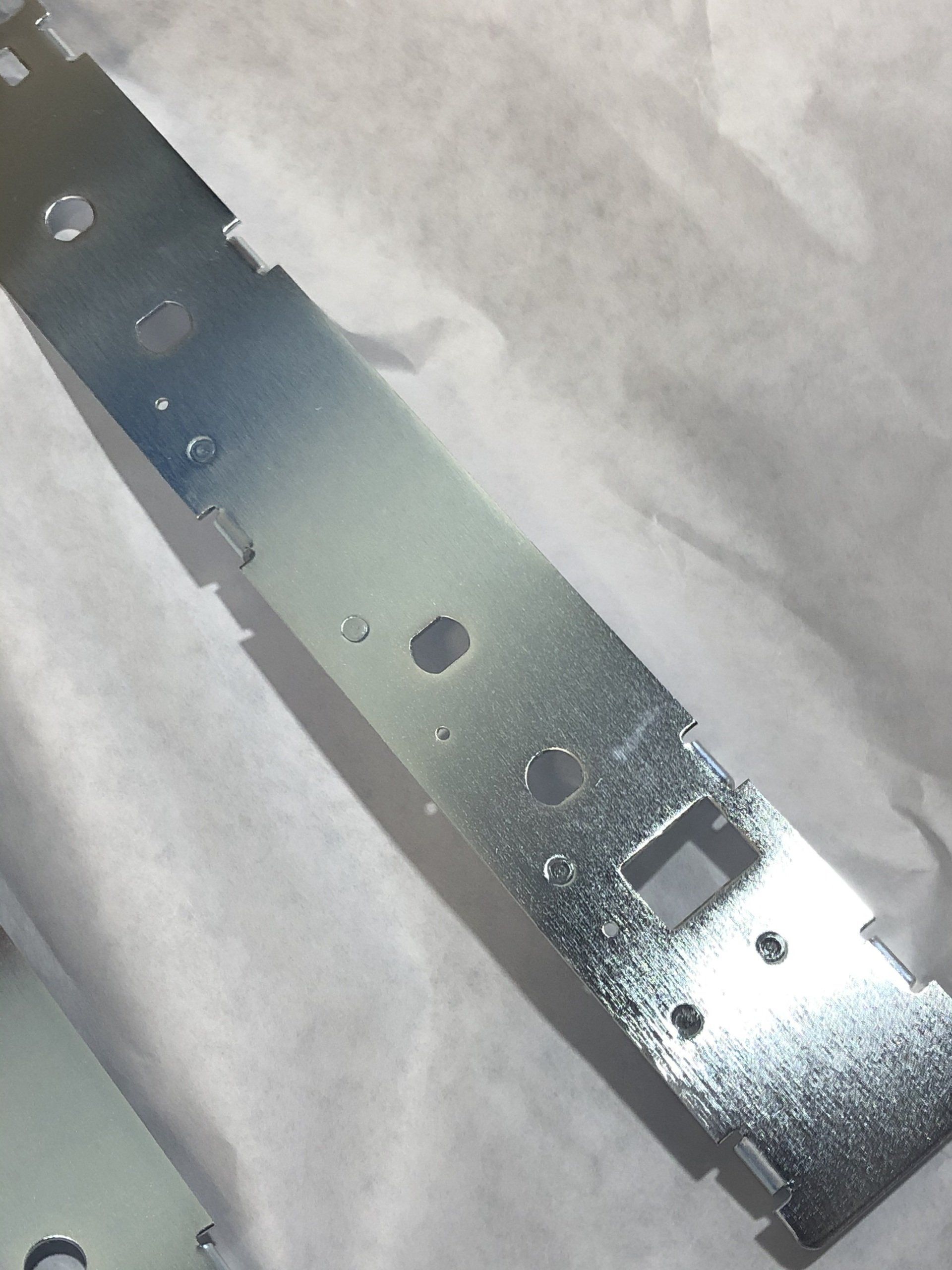 Silver metal bracket with multiple holes and cutouts, resting on a white surface.