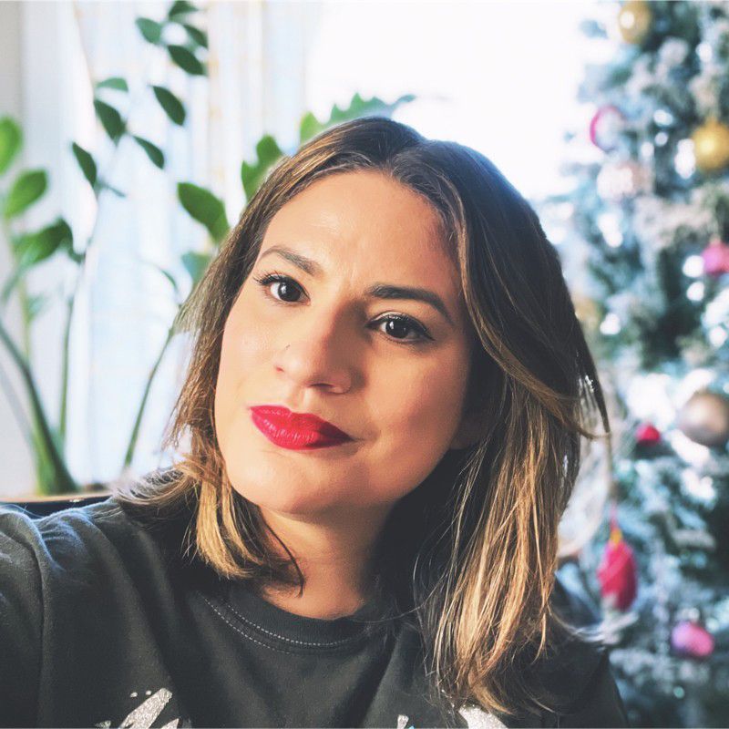 A woman with should-length blonde hair and red lipstick is wearing a dark  shirt