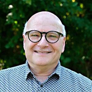 An older man with balding hear and glasses smiling