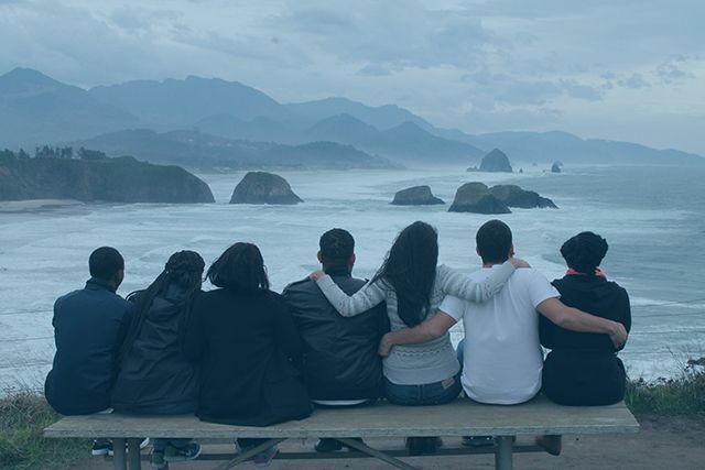 A group of people are sitting on a picnic table looking at the ocean.