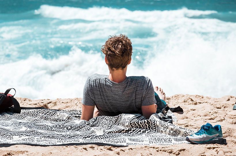A man is laying on a towel on the beach looking at the ocean.