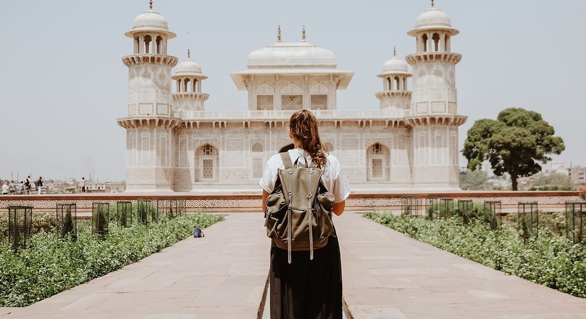 A woman with a backpack is standing in front of a large building.