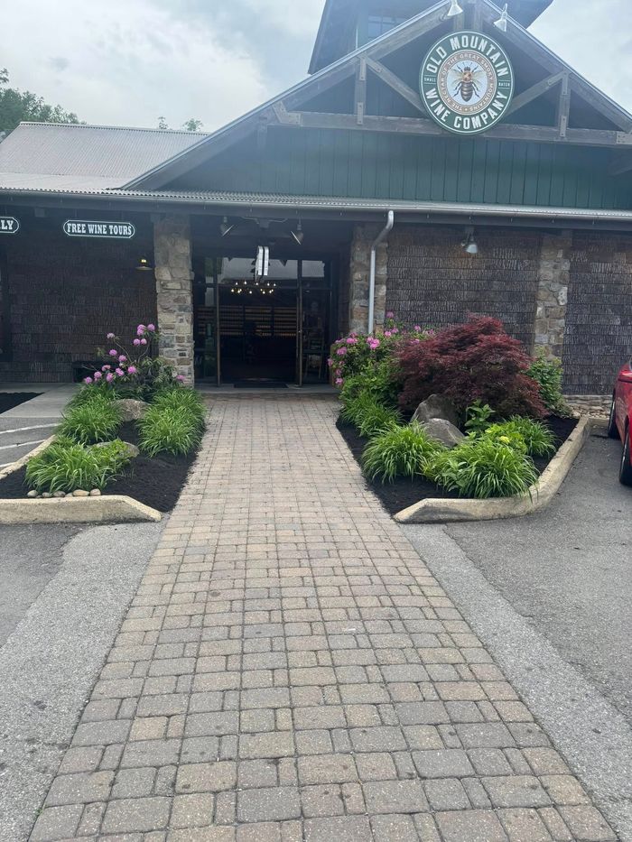 Brick building entrance with central walkway, flower beds, and a clock in the gable above.