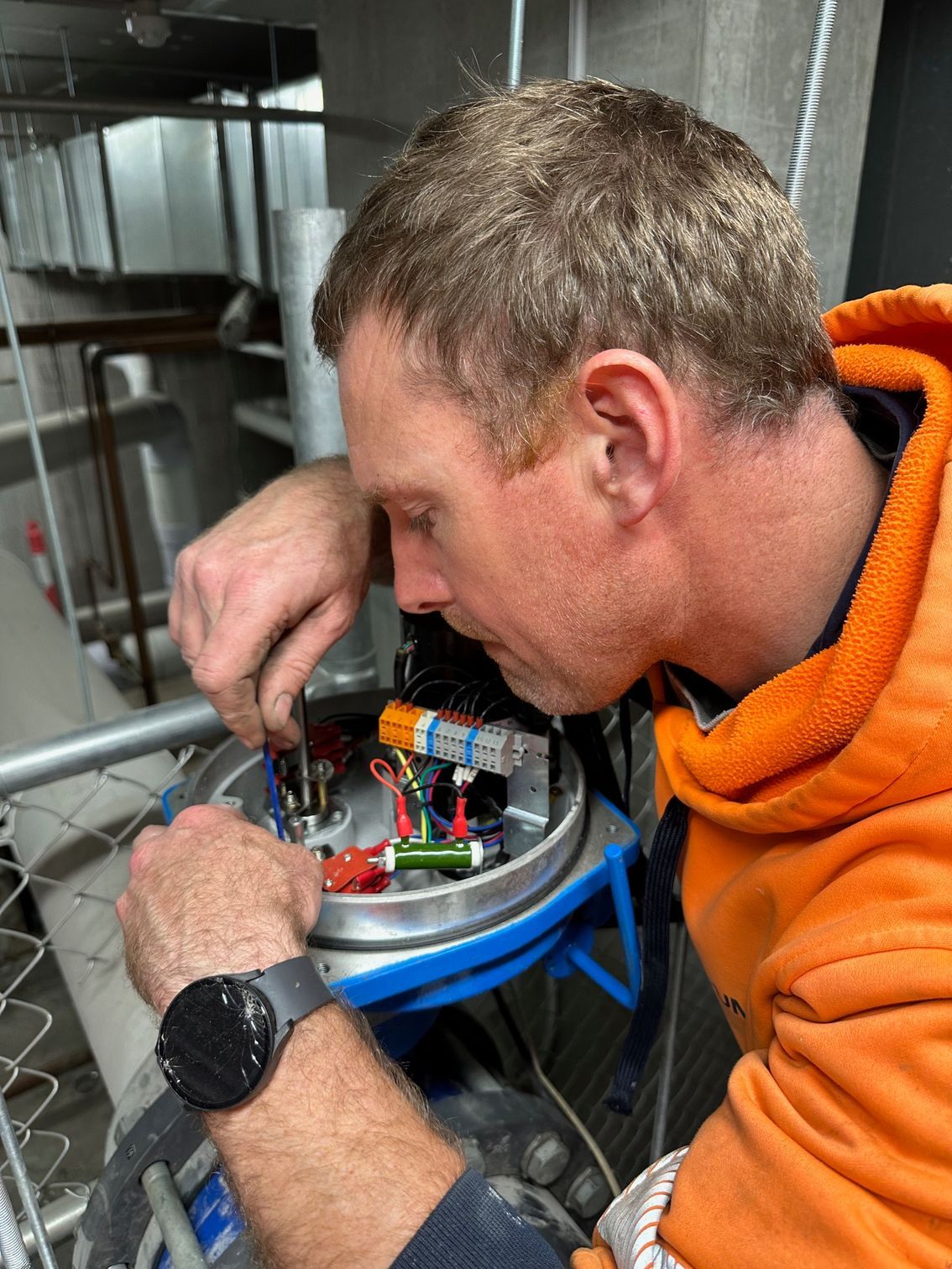 Worker in orange hoodie inspecting wiring inside a metal machine cabinet — PUMPtek in Grovedale, VIC