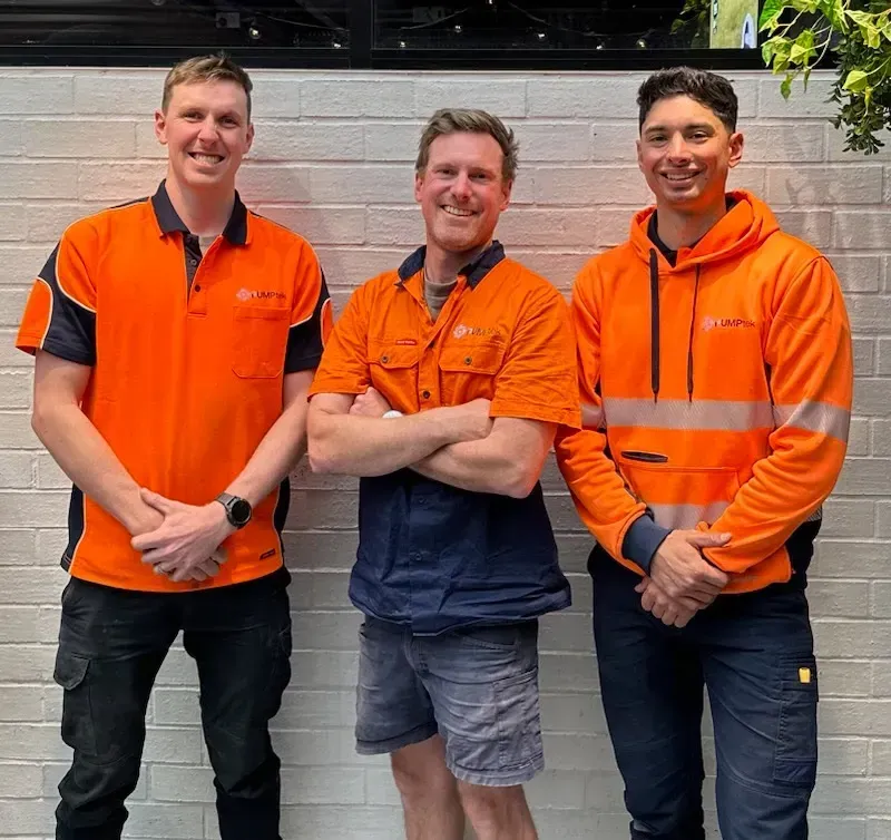 Three People in Orange Work Shirts Posing in Front of a White Brick Wall — PUMPtek in Grovedale, VIC
