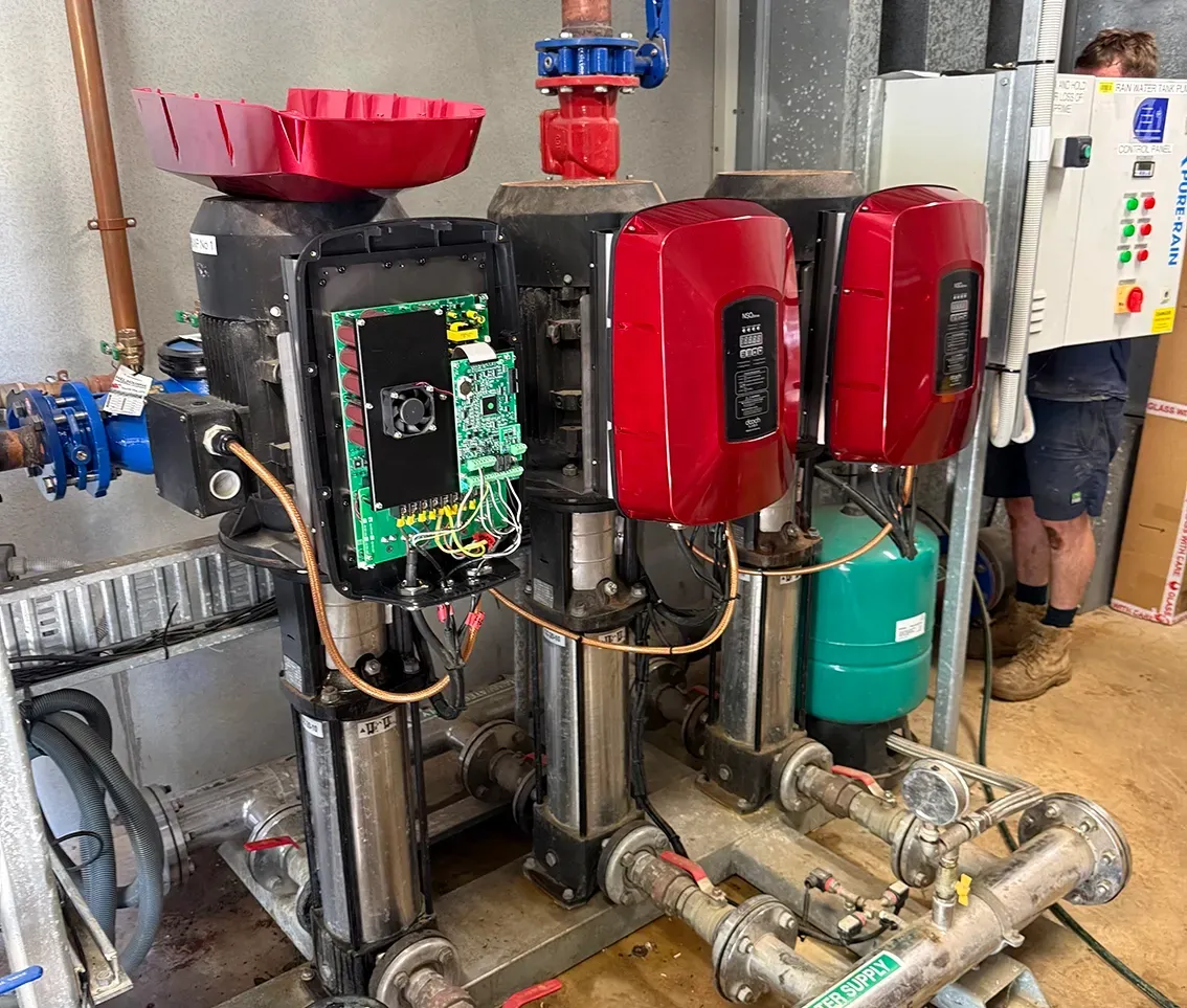 Industrial pump room with red and black pumps, exposed wiring, and a technician working in the background — PUMPtek in Bendigo, VIC
