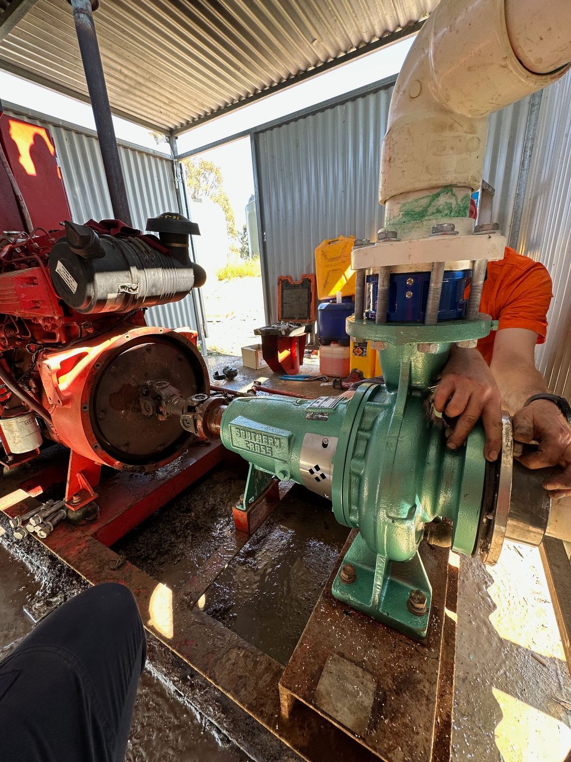 Mechanic working on a green industrial pump beside a red engine in a covered workshop — PUMPtek in Grovedale, VIC