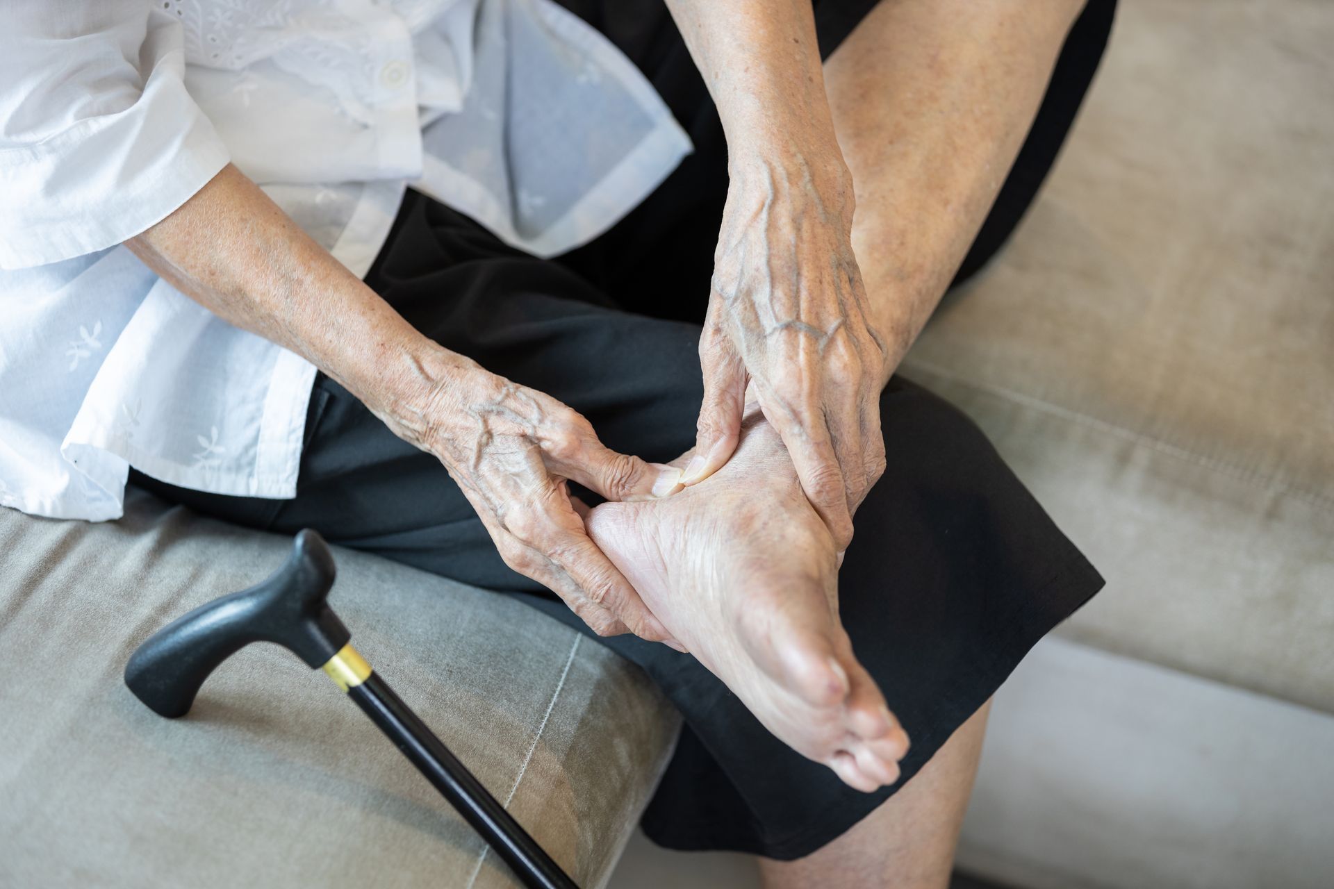 Person seated, holding foot and ankle, cane nearby.