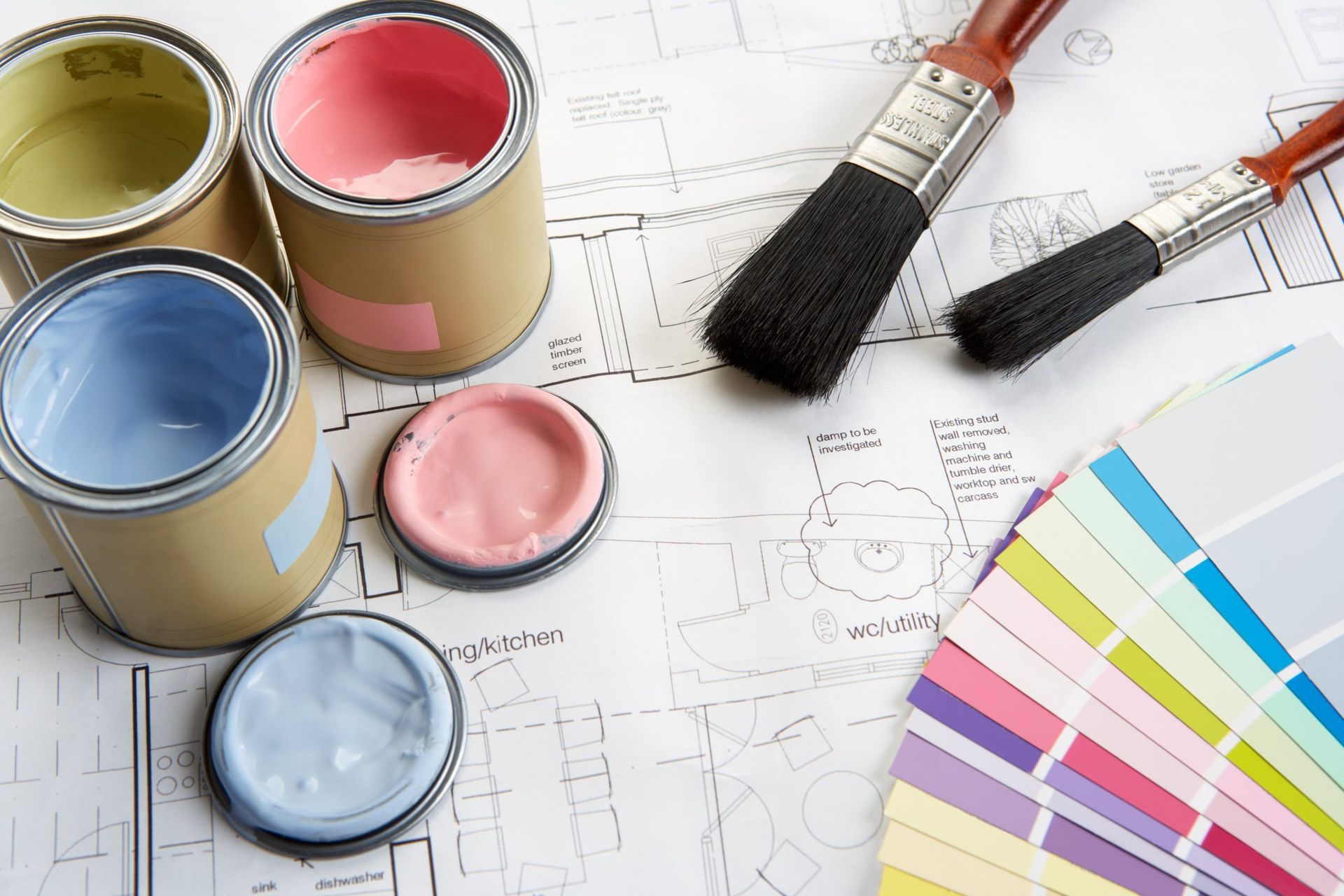 Paint cans, brushes, and a color palette swatch fan resting on top of architectural blueprints.