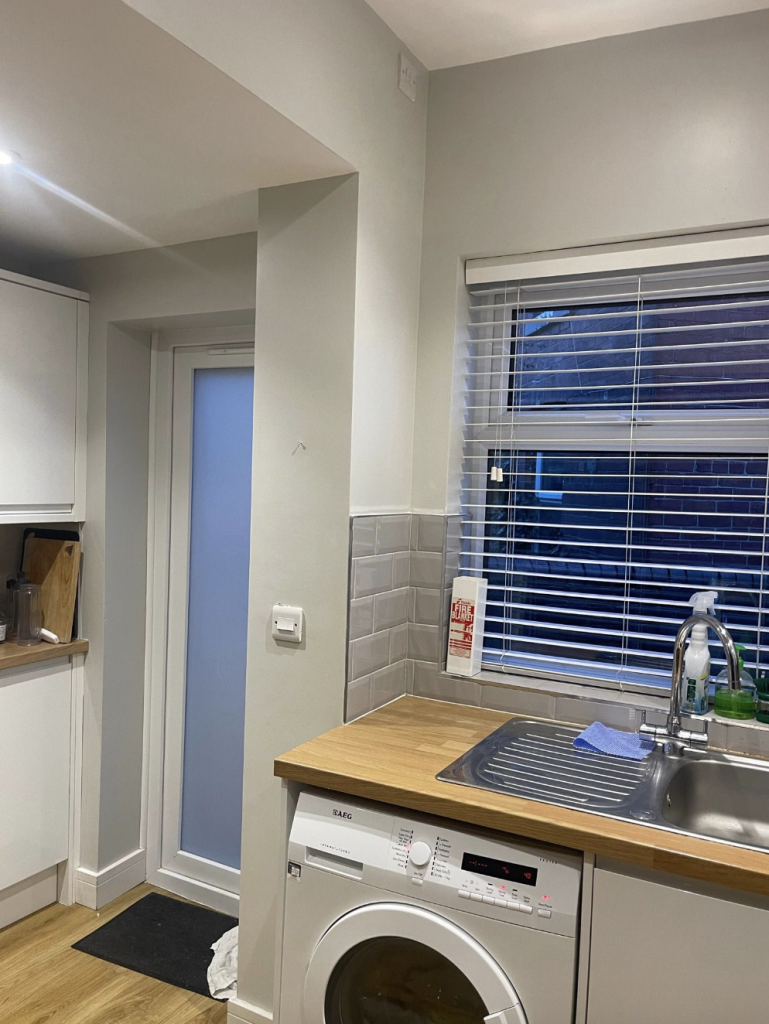 A corner of a kitchen with light grey walls, white cabinets, a wood countertop, a washing machine, and a frosted door.