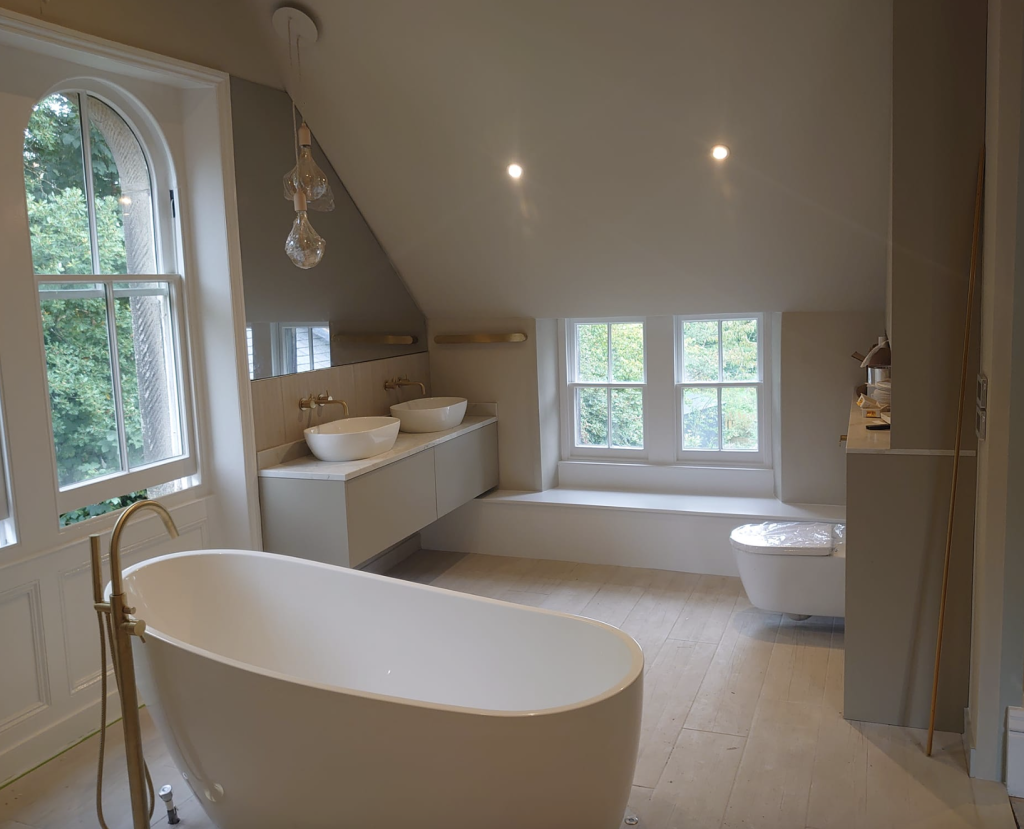 A contemporary attic bathroom with a white freestanding tub, dual vanity, and a toilet under a sloping ceiling.