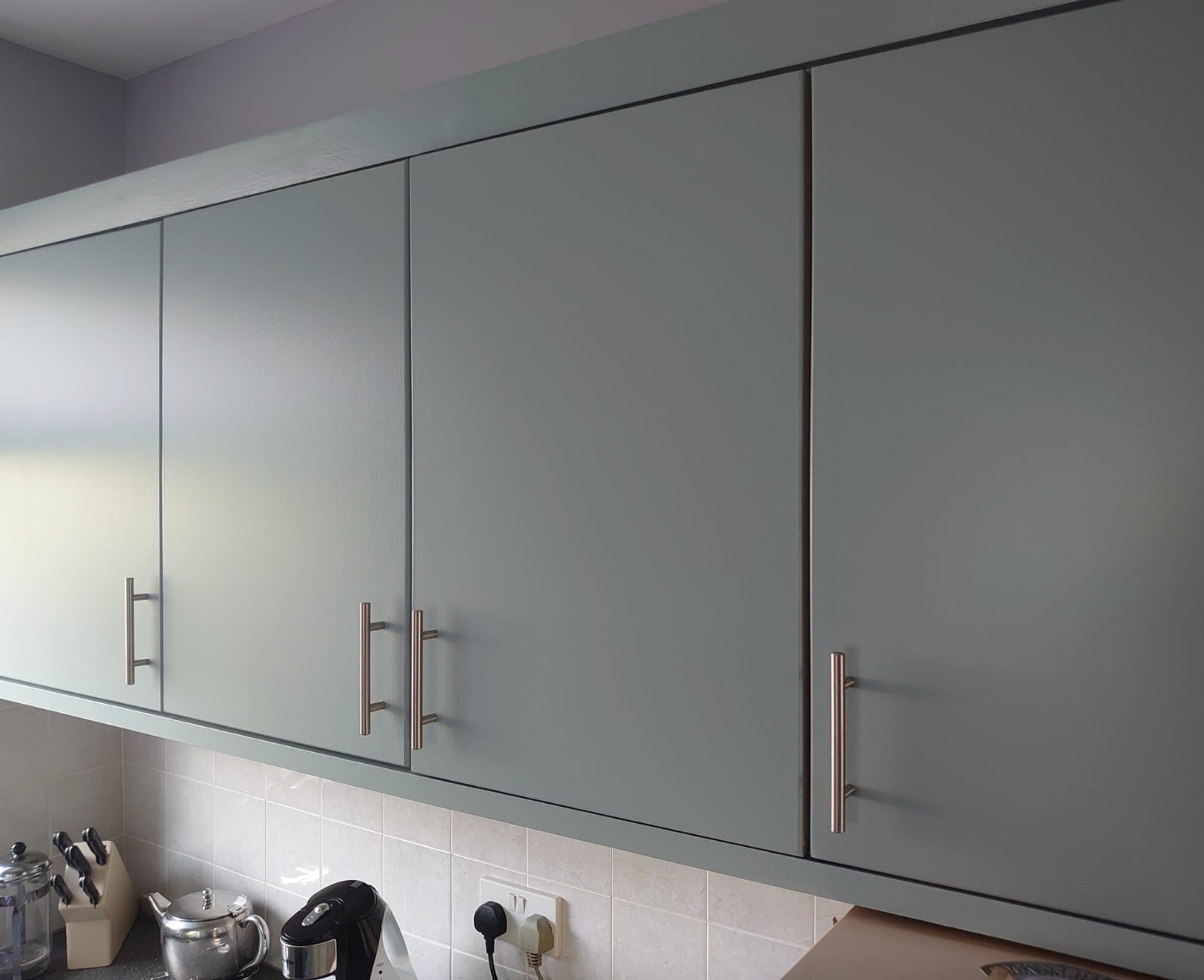 Gray kitchen cabinets with silver bar handles, positioned above a tiled backsplash and kitchen counter.
