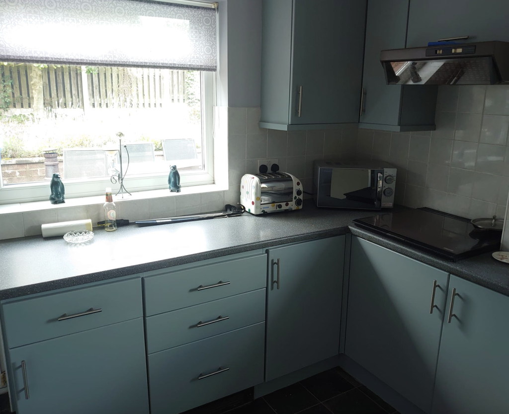 A kitchen featuring grey cabinets, a window with a roller blind, a toaster, and a microwave on the counter.