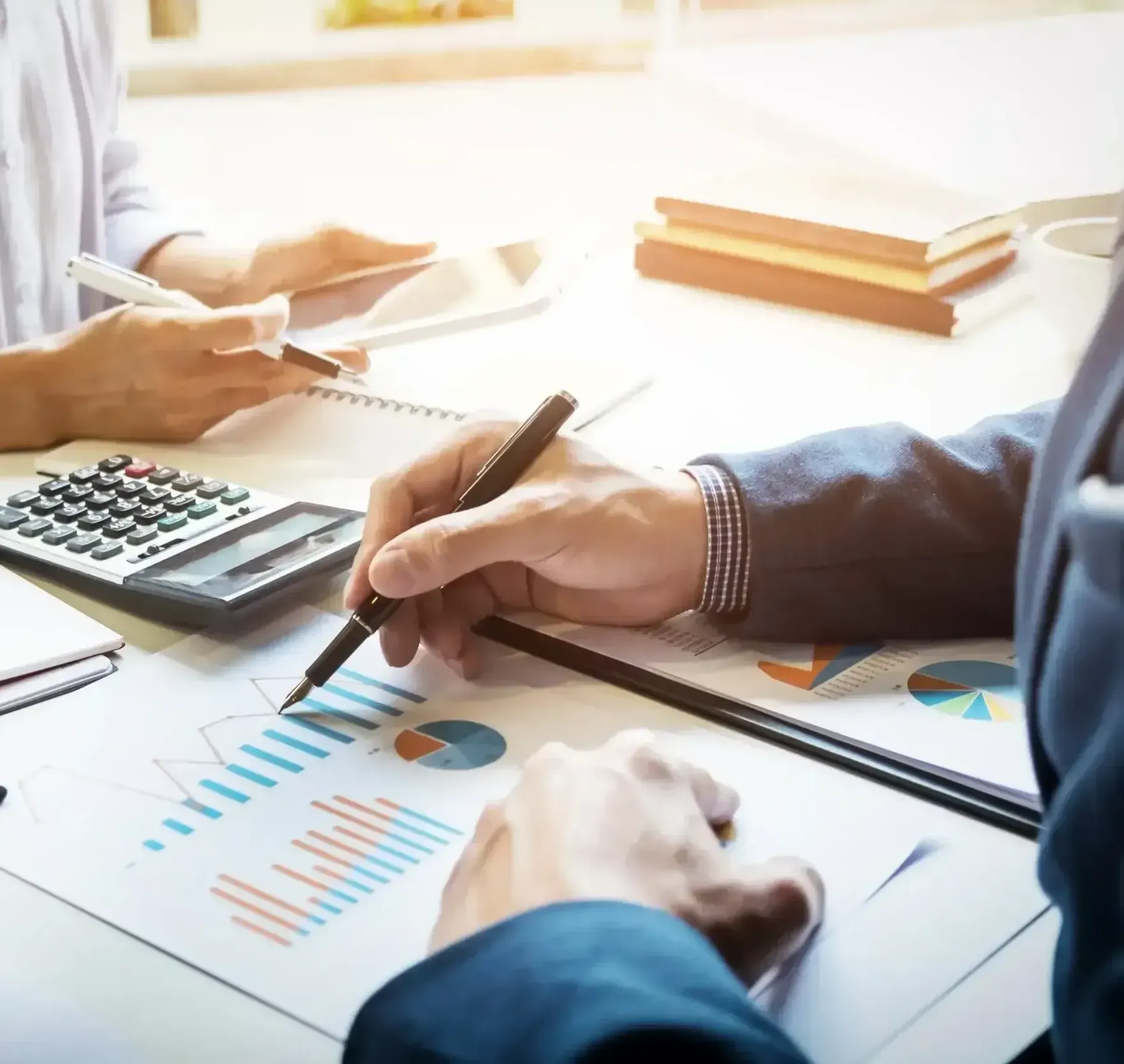 Two people at a desk review financial charts, using a calculator and tablet.
