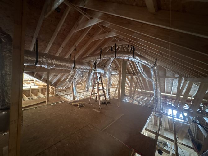 Attic interior showing unfinished wooden rafters and multiple flexible insulated air ducts hanging from the framing.
