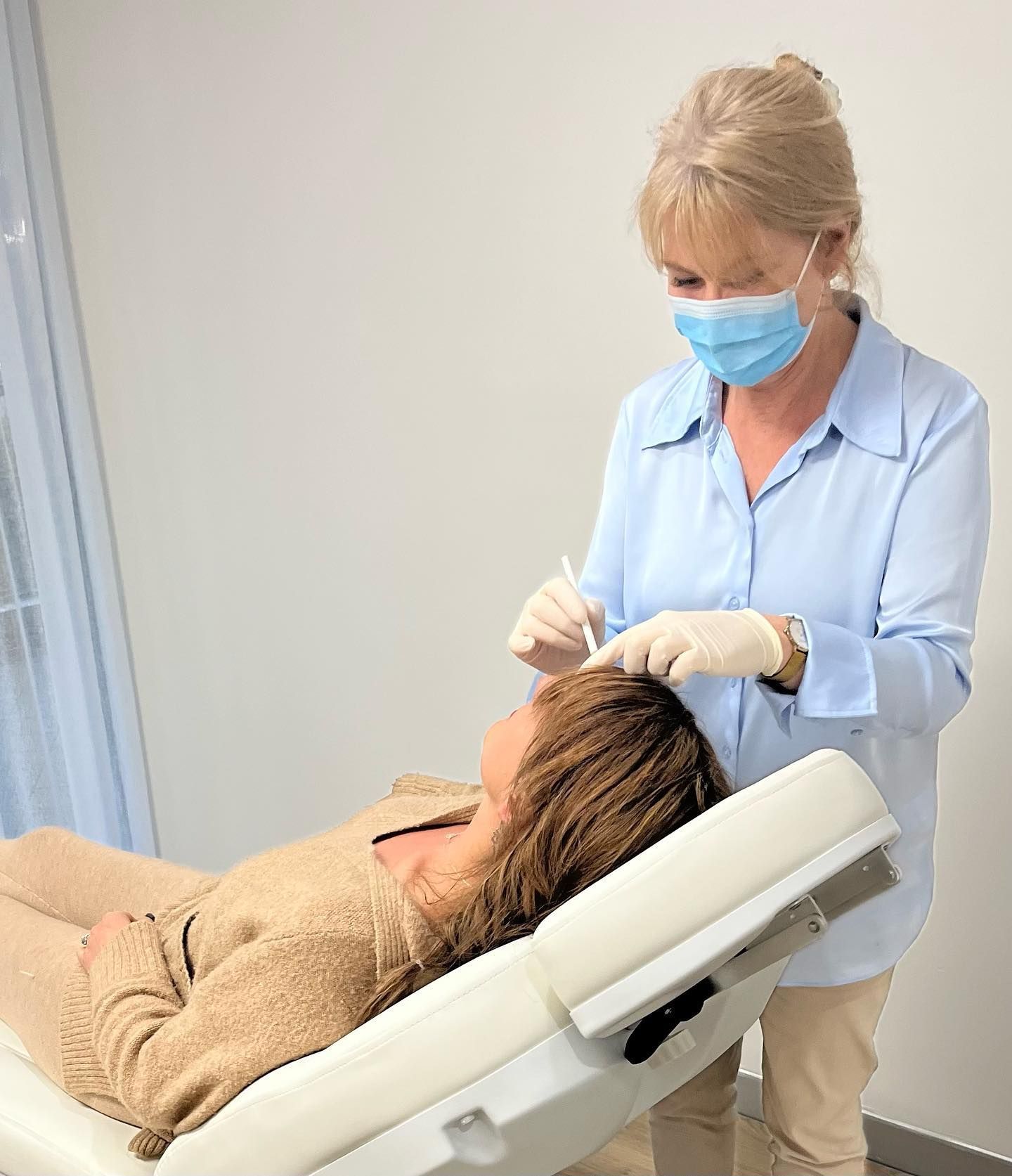 A wOman Wearing a Mask and Gloves is Standing Next to a Woman Laying in a Chair — Aura Mediclinic in Ashmore, QLD