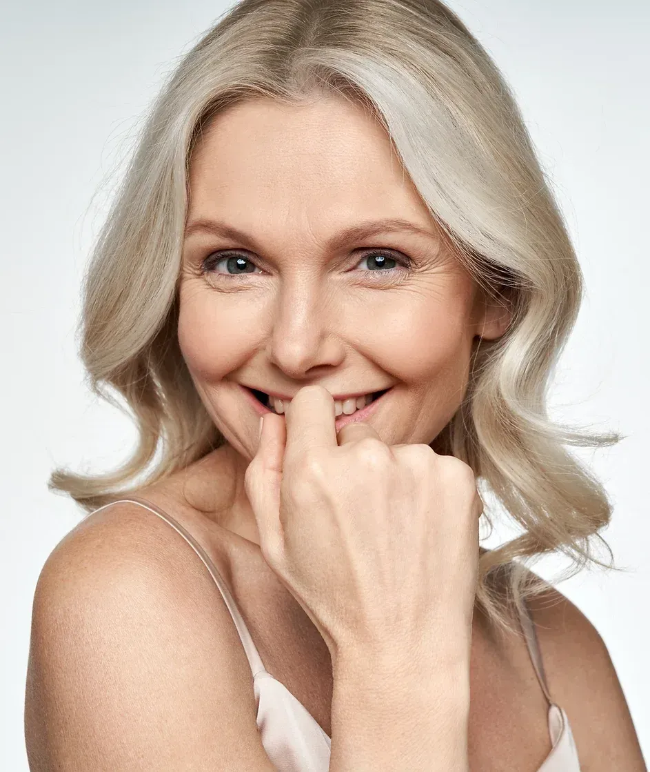 A Woman With Blonde Hair is Smiling and Holding Her Hand to Her Face — Aura Mediclinic in Ashmore, QLD