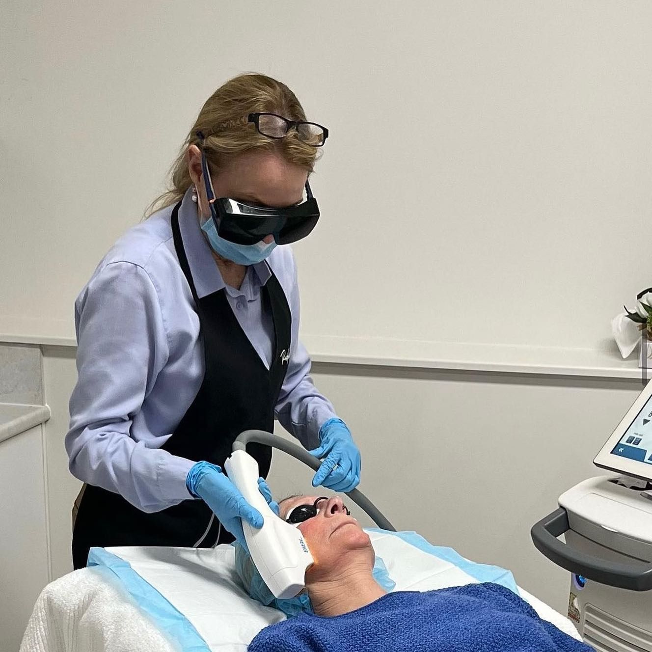 A Woman Wearing a Mask and Goggles is Using a Machine on a Patient's Face — Aura Mediclinic in Varsity Lake, QLD