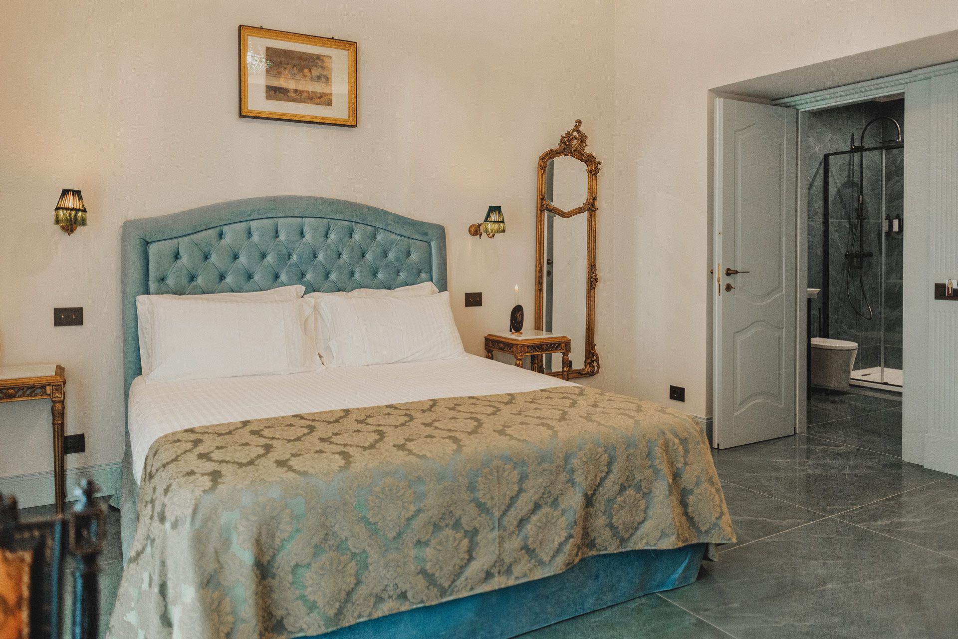 Camera da letto con letto blu trapuntato, copriletto a fantasia, lampade da parete e porta aperta che conduce al bagno.