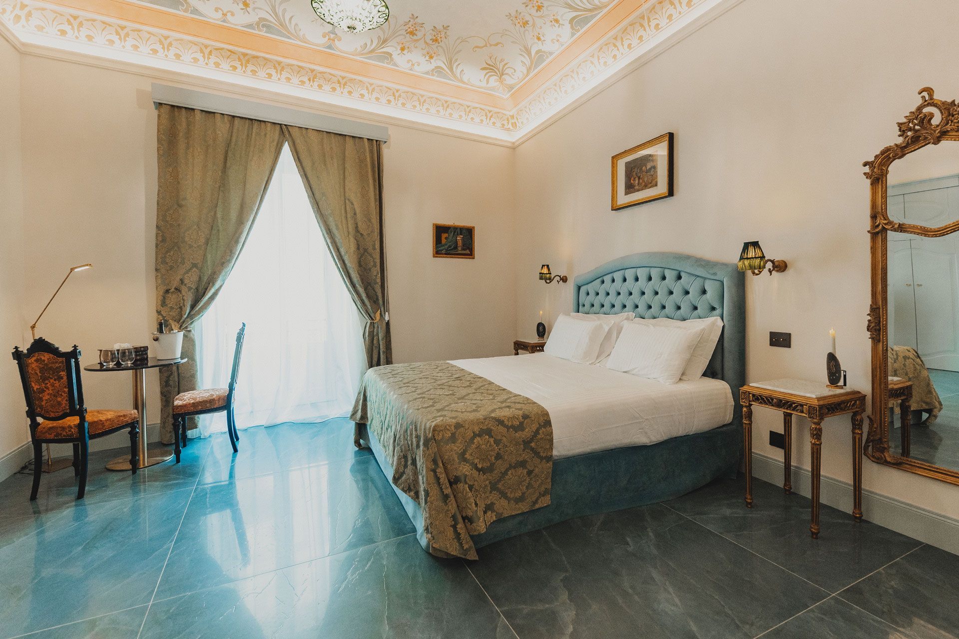 Luminosa camera da letto in stile hotel con letto color verde acqua, finestra con tende, scrivania e specchio decorato.