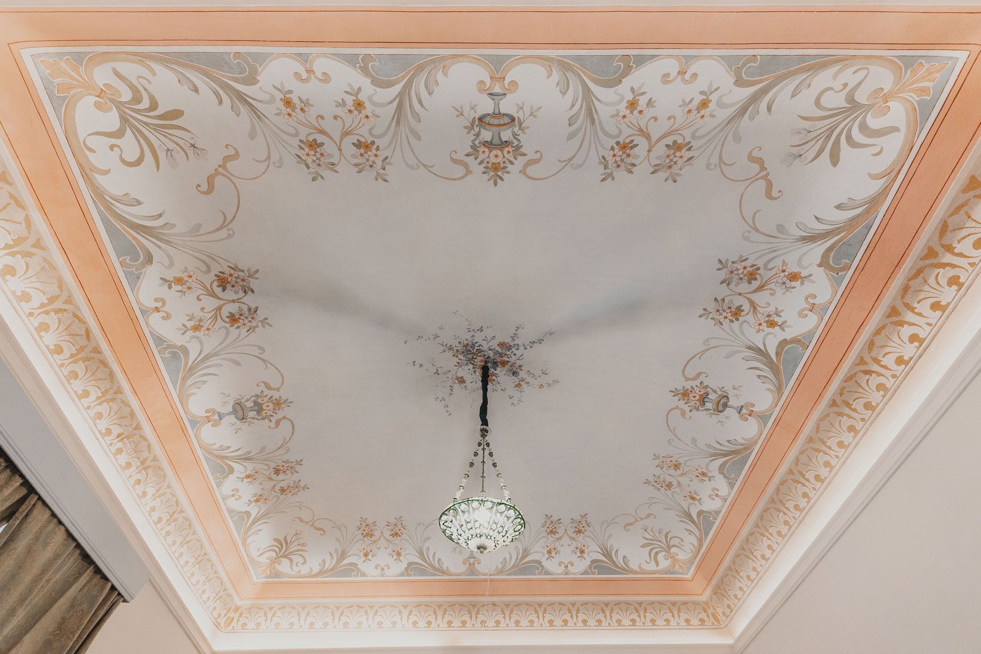 Soffitto decorato con bordo color pesca e oro e lampadario a sospensione, che mostra macchie di fumo o fuliggine al centro.