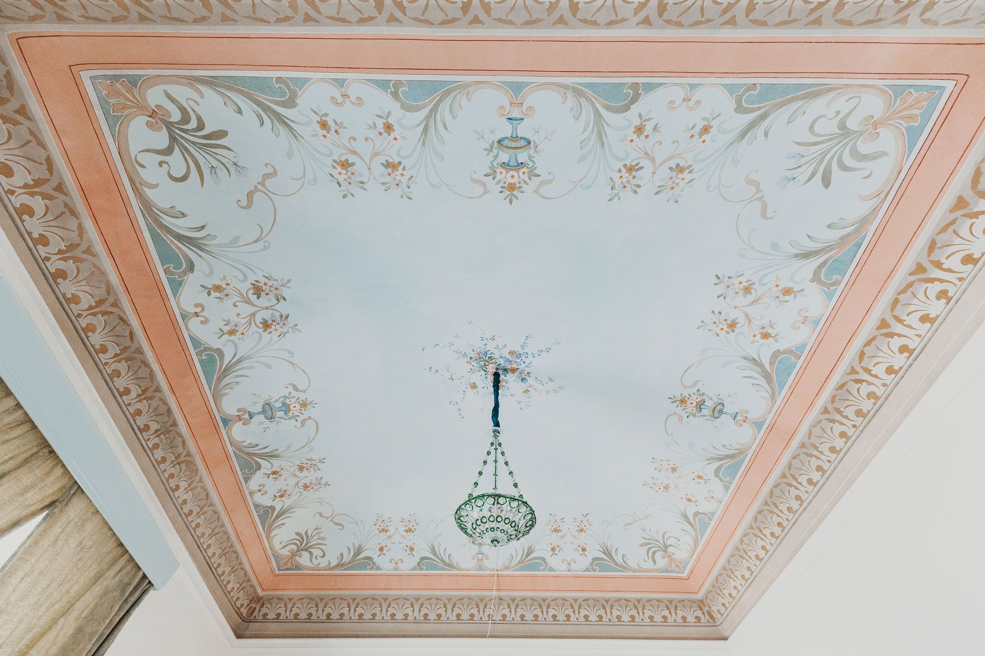 Soffitto decorato con motivi pastello, bordo floreale e lampadario a sospensione in vetro verde.