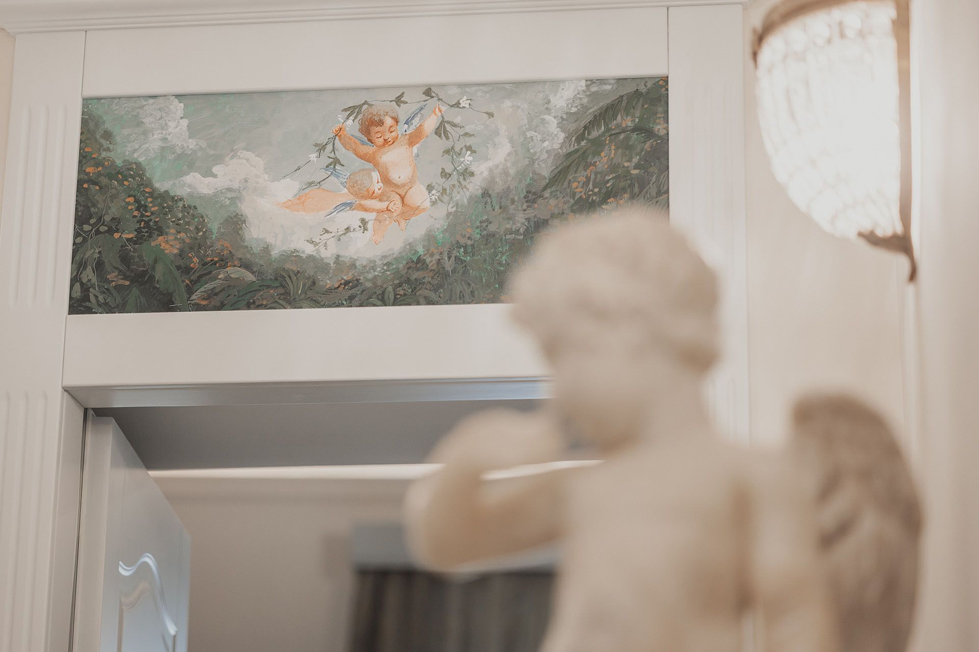 Statua bianca sfocata in primo piano sotto un pannello decorativo floreale sopra una porta.