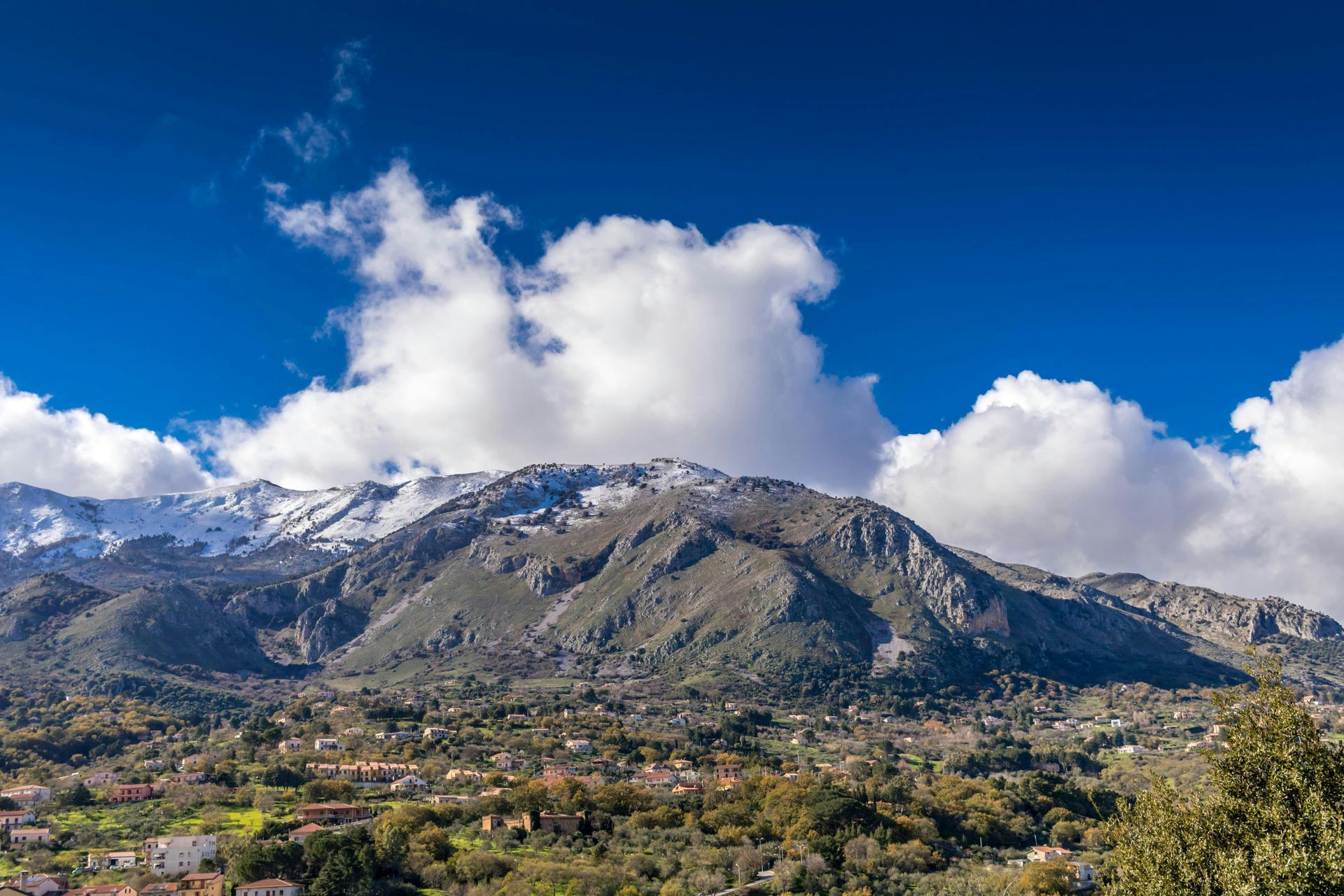 Montagna innevata sotto un cielo azzurro brillante sopra una verde vallata e una piccola città