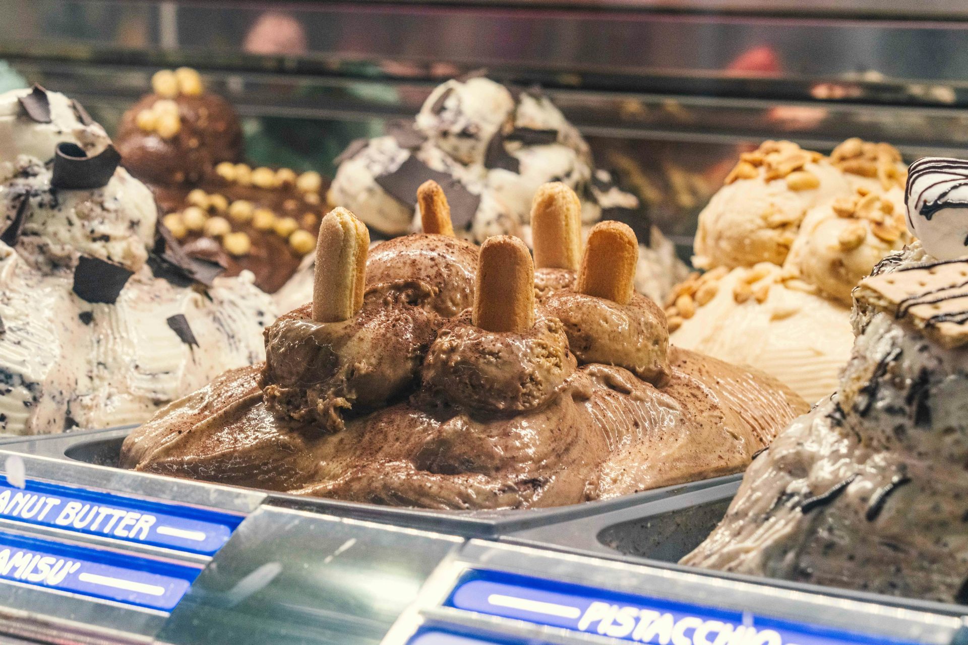 Vetrina per gelati con diversi gusti, tra cui cioccolato e vaniglia, in una teca di vetro.
