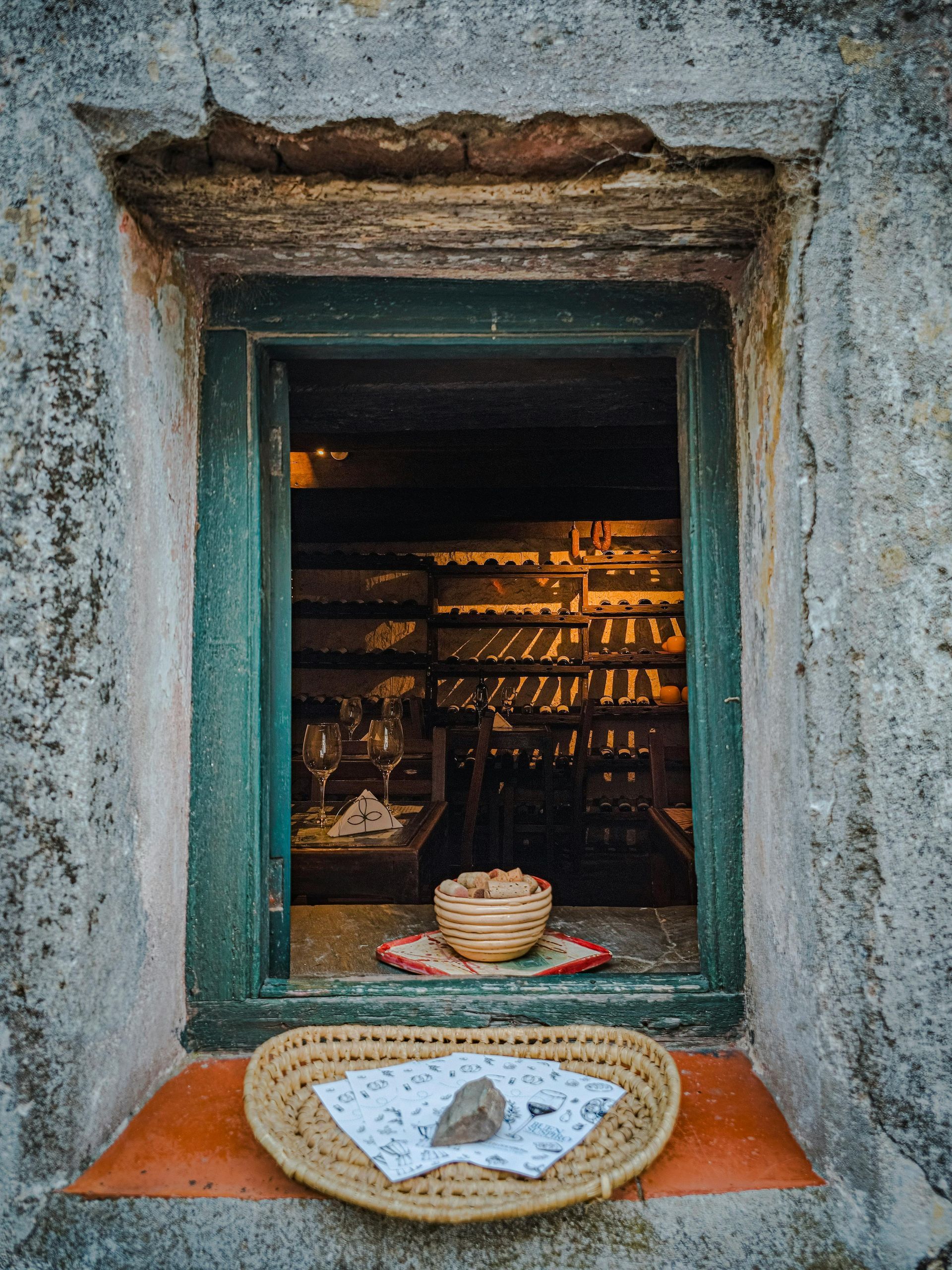 Finestra rustica con cesti intrecciati su una mensola di pietra, che lascia intravedere un interno illuminato 
