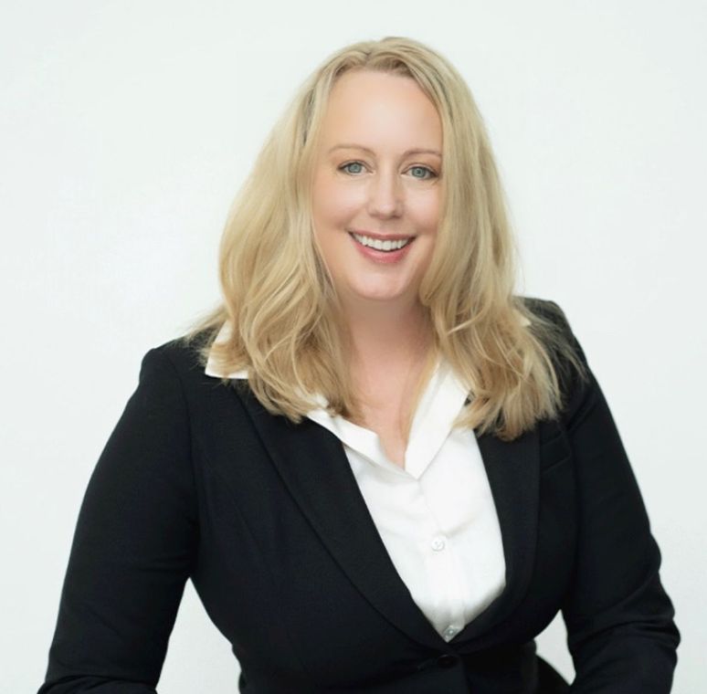 A woman in a black jacket and white shirt smiles for the camera