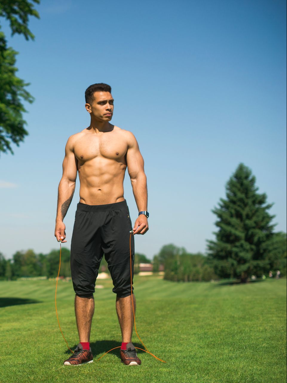 A shirtless man is jumping a jump rope in a park.