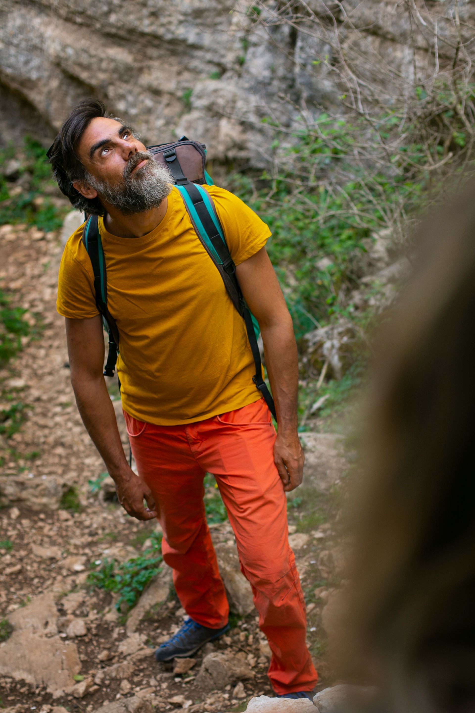 A man with a backpack is standing on a rocky path looking up.