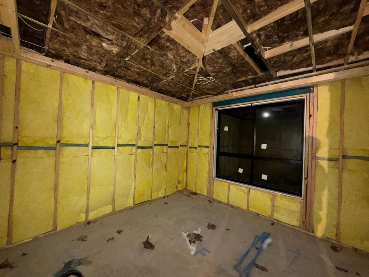 Insulated unfinished room with exposed framing, bare floor, and windows along one wall