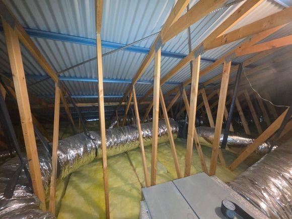 Attic with wooden rafters and a thick layer of gray blown-in insulation around a support post