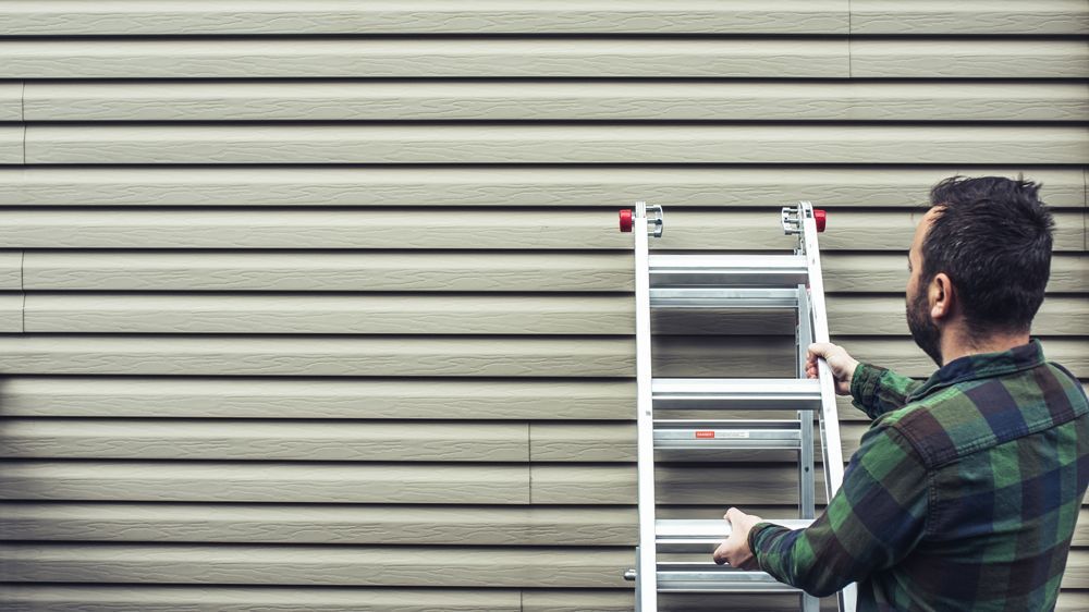 Man Holding To The Ladder on The Siding — Hudson, MI — D & C Roofing