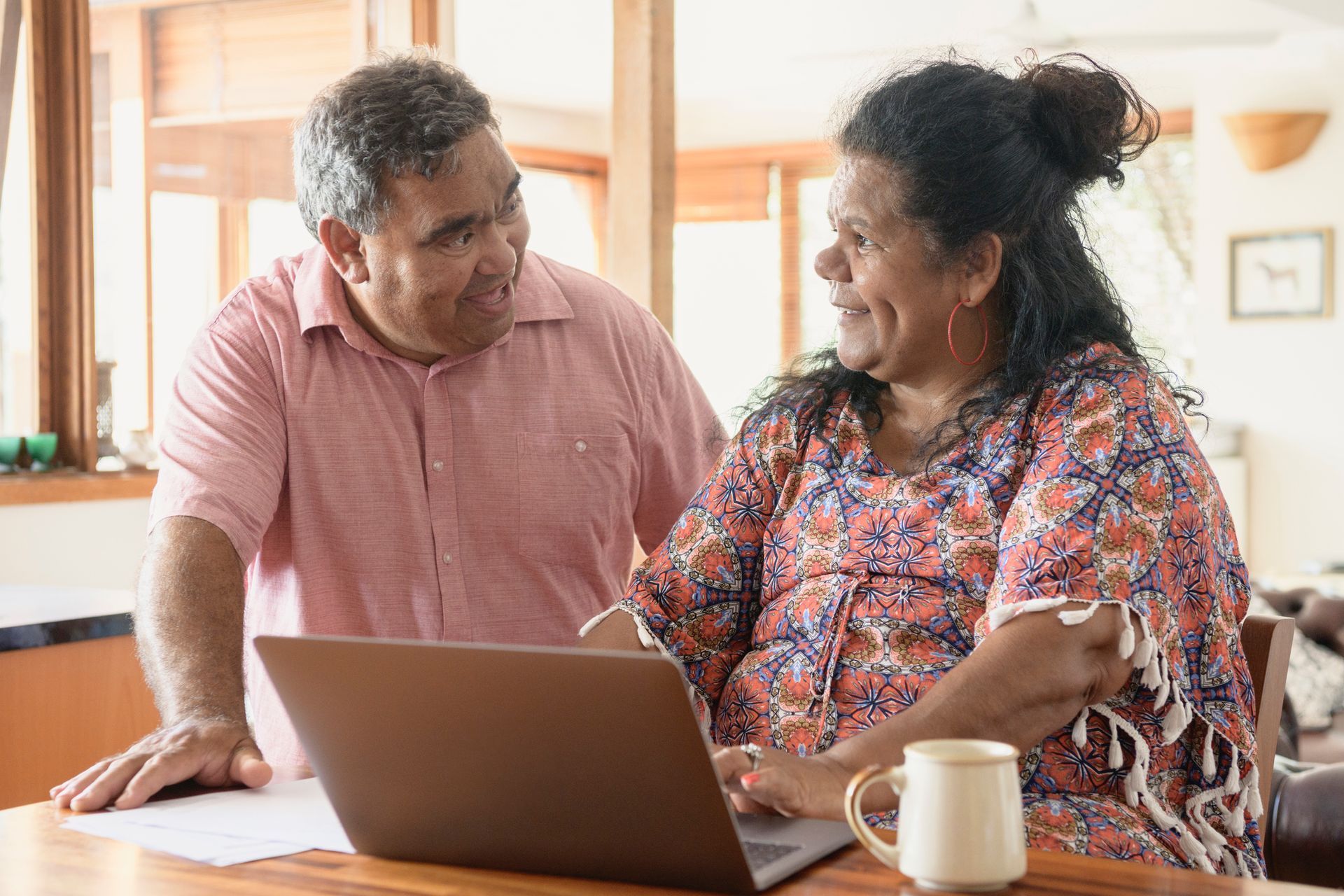 A man and a woman are sitting at a table looking at a laptop computer.