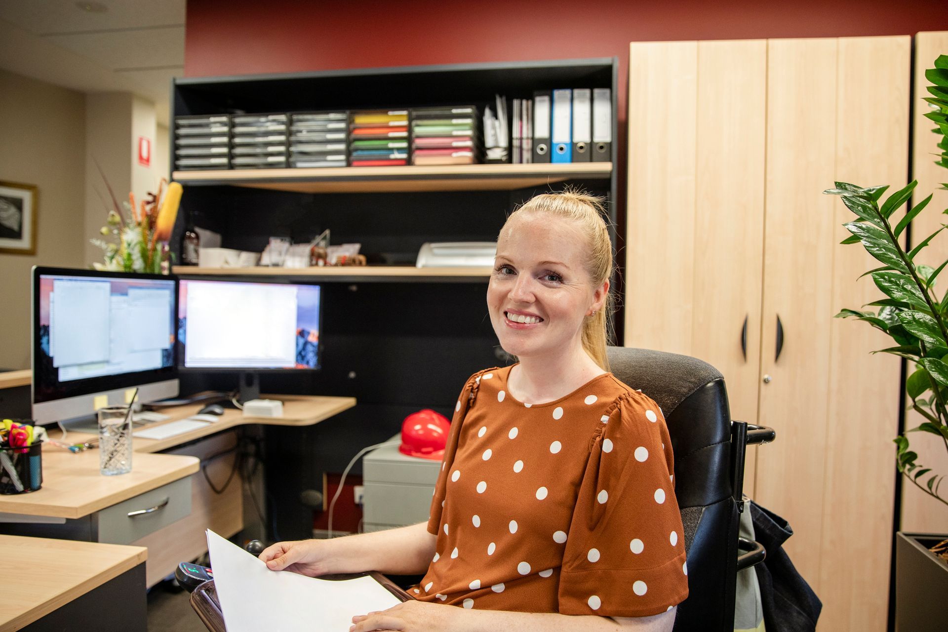 A woman in a wheelchair is sitting at a desk in an office.