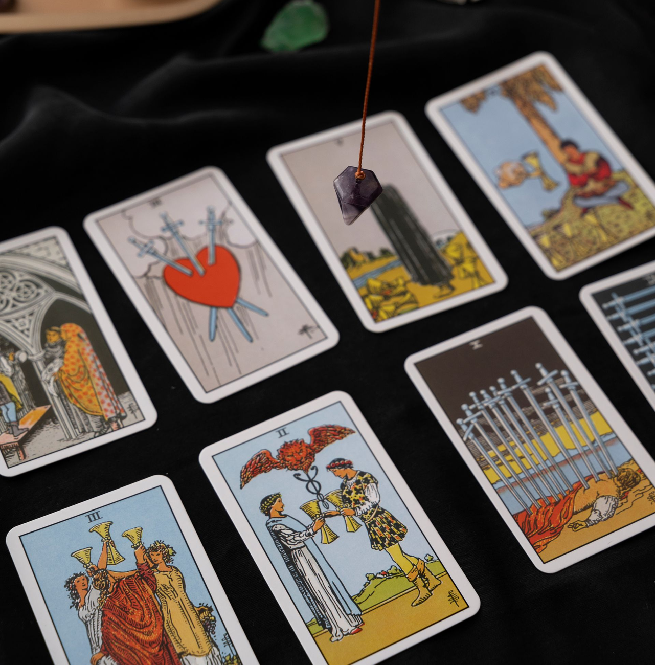 Cartas del tarot extendidas sobre un paño oscuro, con un péndulo suspendido sobre las cartas centrales.