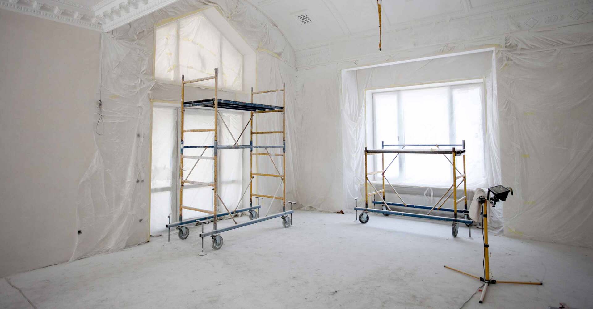 Room being renovated, scaffolding, plastic sheeting on walls and windows.